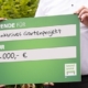 Das Foto zeigt einen Ausschnitt des Fotos der Pressemitteilung. Hände halten einen Scheck der VR Bank Niederbayern-Oberpfalz eG mit einer Spendensumme von 2000 Euro.